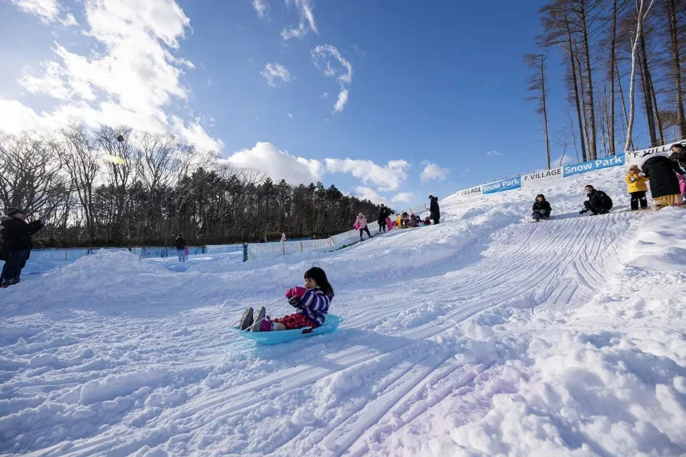 雪山で遊ぶ子供たちの写真。青いそりに乗って滑っている女の子がいます。