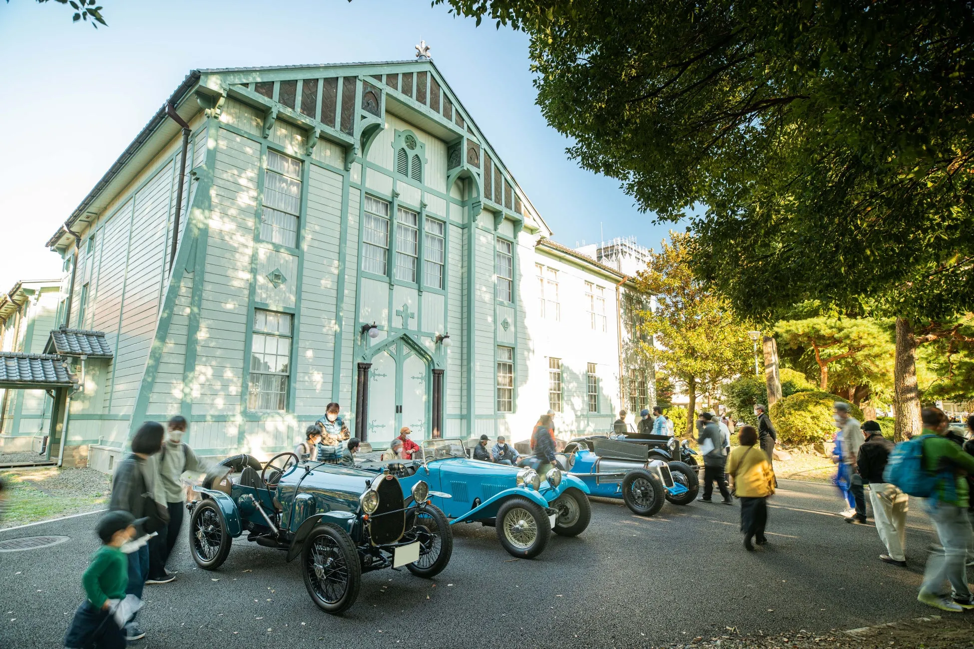 クラシックカーが並び、人々が集まるイベントの様子。背景には歴史的な建造物があり、イベントの雰囲気を引き立てています。