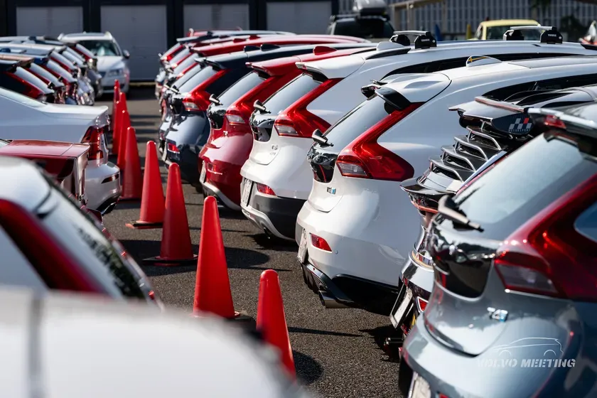駐車場に駐車されたさまざまな色の車の列のクローズアップショット。オレンジ色の交通安全コーンが車の後ろに立っている。