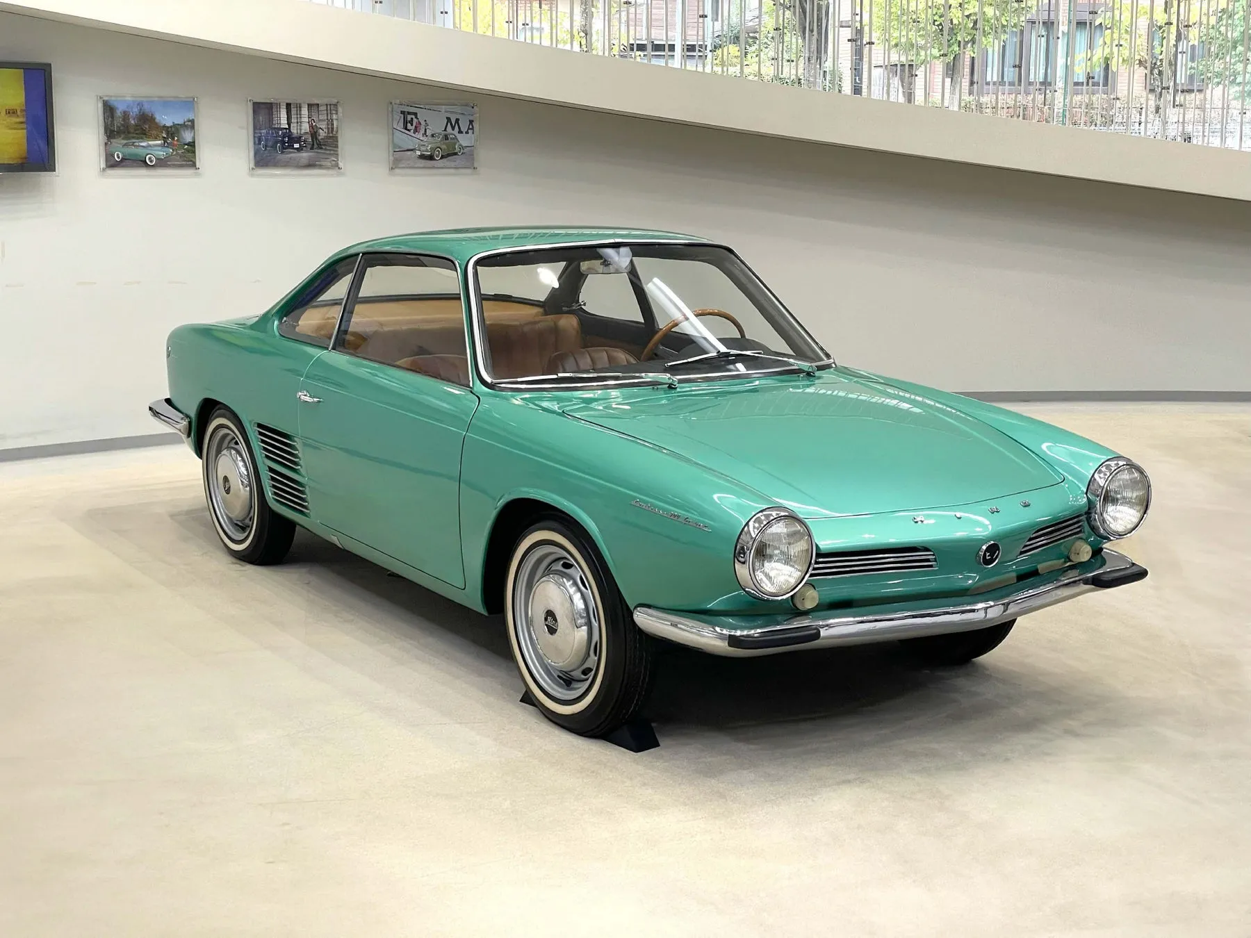 水色のクラシックカーの写真。車は展示スペースにあり、背景には絵画が飾られている。