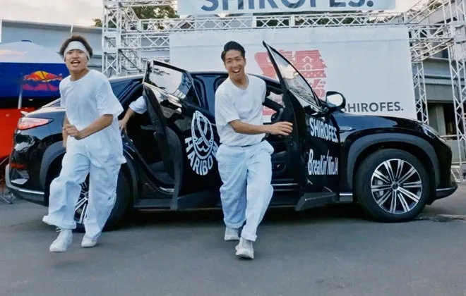 2人の男性が黒い車から出てきて、カメラに向かって走っている様子。車には「SHIROFES」と「HARIBO」のロゴが入っており、イベントの宣伝のようだ。