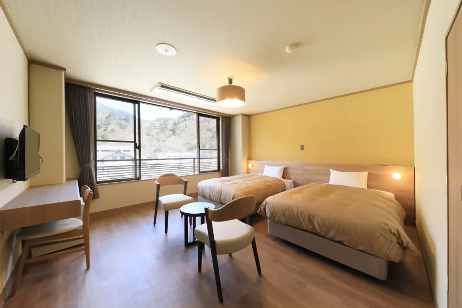 2つのベッドと窓、椅子、テーブルがあるホテルの部屋