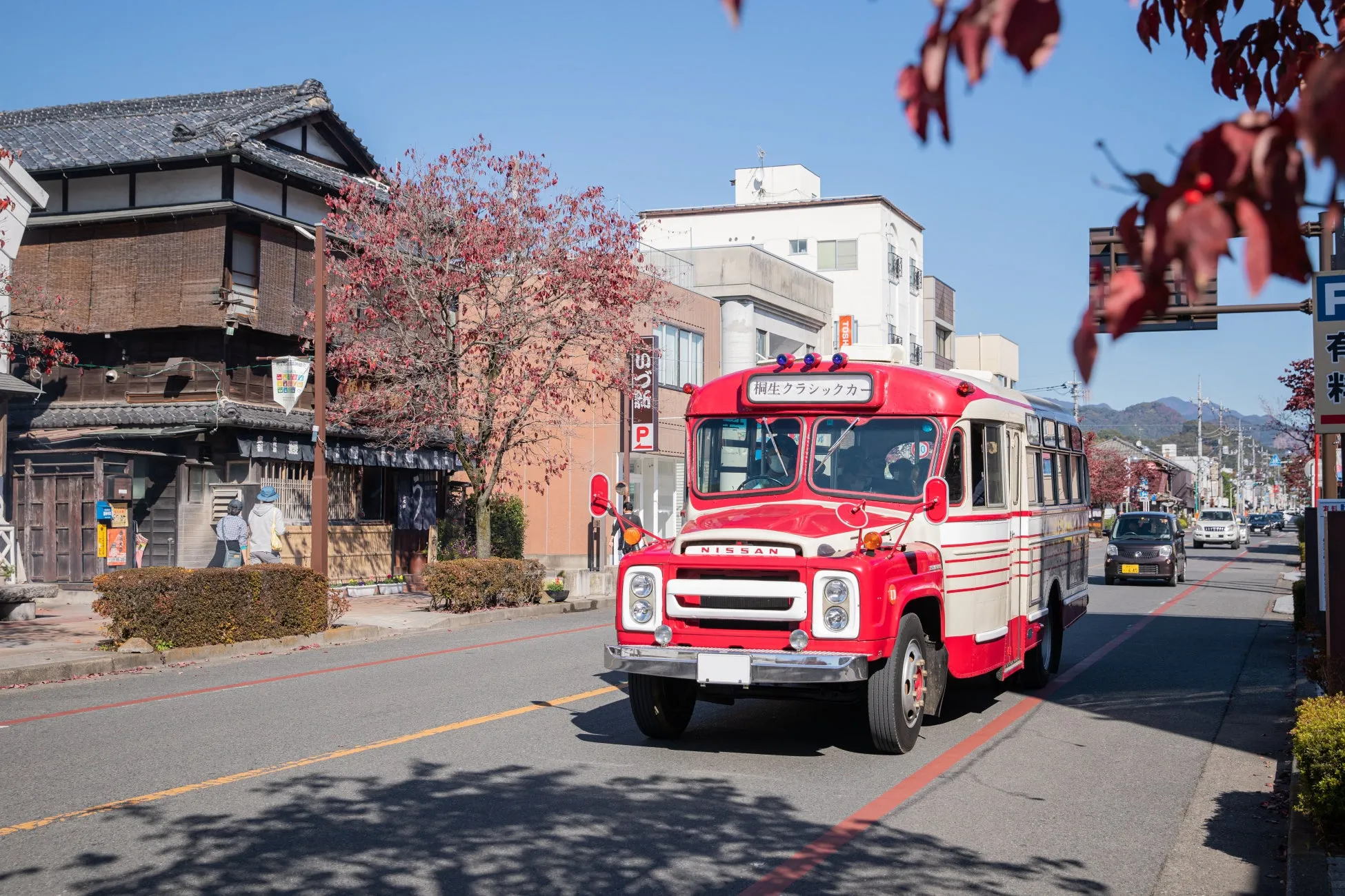 レトロな赤いバスが日本の街並みを走っている様子。