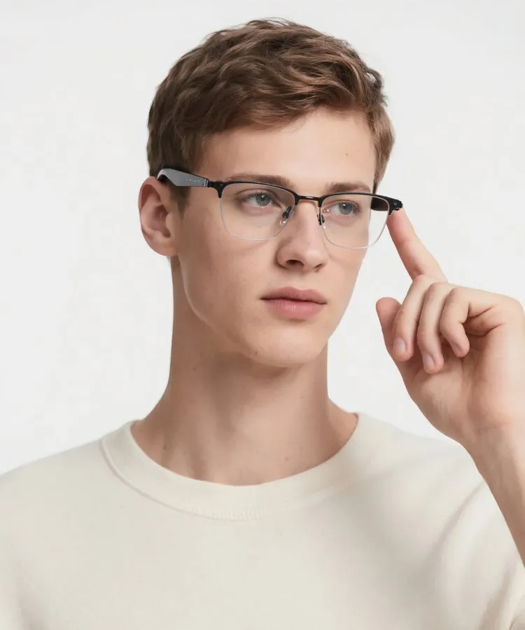 眼鏡をかけた男性のポートレート。男性は白いセーターを着ており、眼鏡に指をかけている。