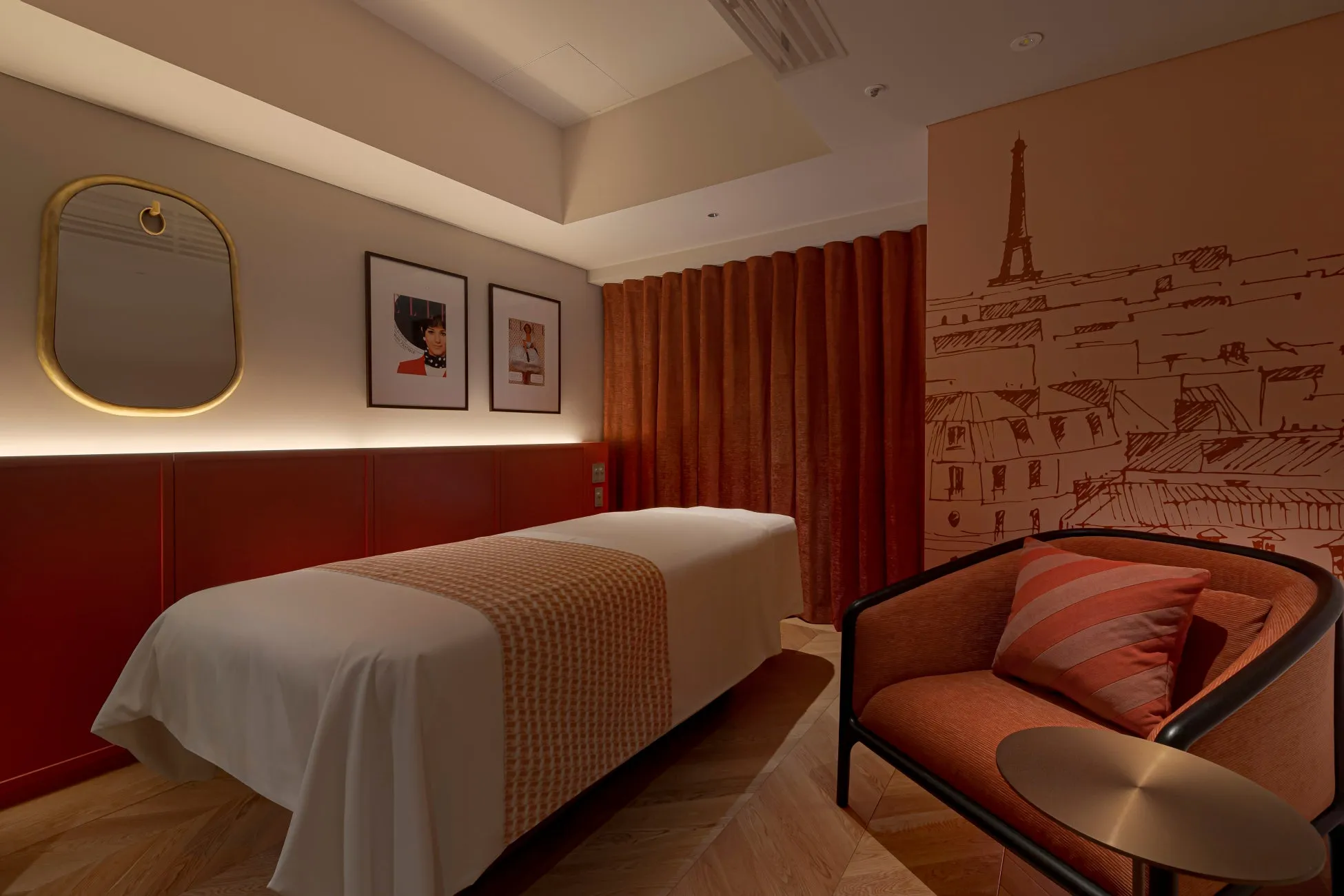 パリをテーマにしたスパルーム。エッフェル塔の壁画、マッサージベッド、椅子、鏡。