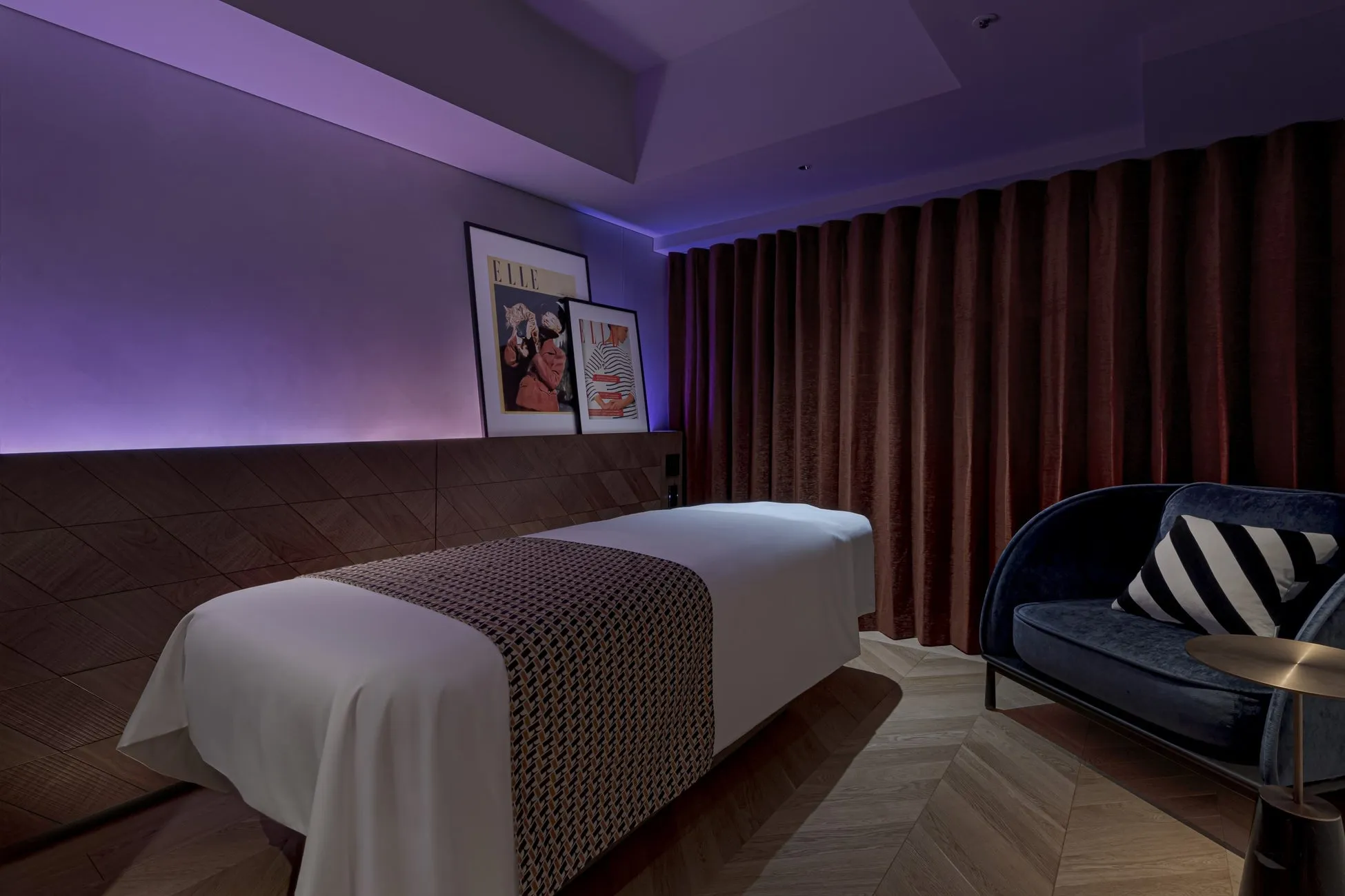 スパルームのインテリア。ベッド、クッション付きのソファ、カーテン、アートワークが特徴。