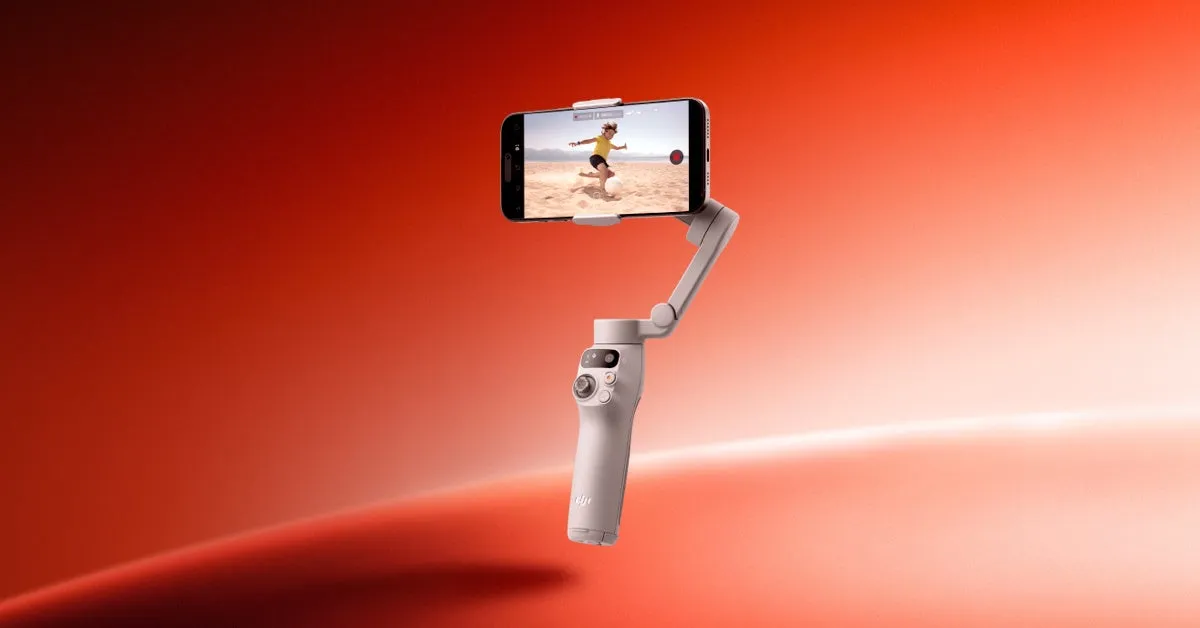 スマートフォンを装着したジンバル。画面には人が砂浜でボールを蹴る様子が映し出されている。ジンバルは白く、背景は赤色。