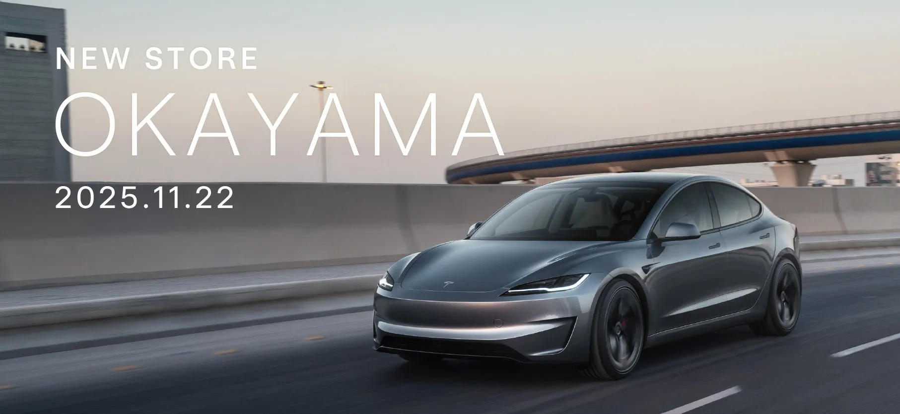 テスラの新店舗オープンの告知画像。グレーのテスラ車が道路を走行しており、背景には都市の風景が広がっています。「NEW STORE OKAYAMA 2025.11.22」というテキストが大きく表示されています。
