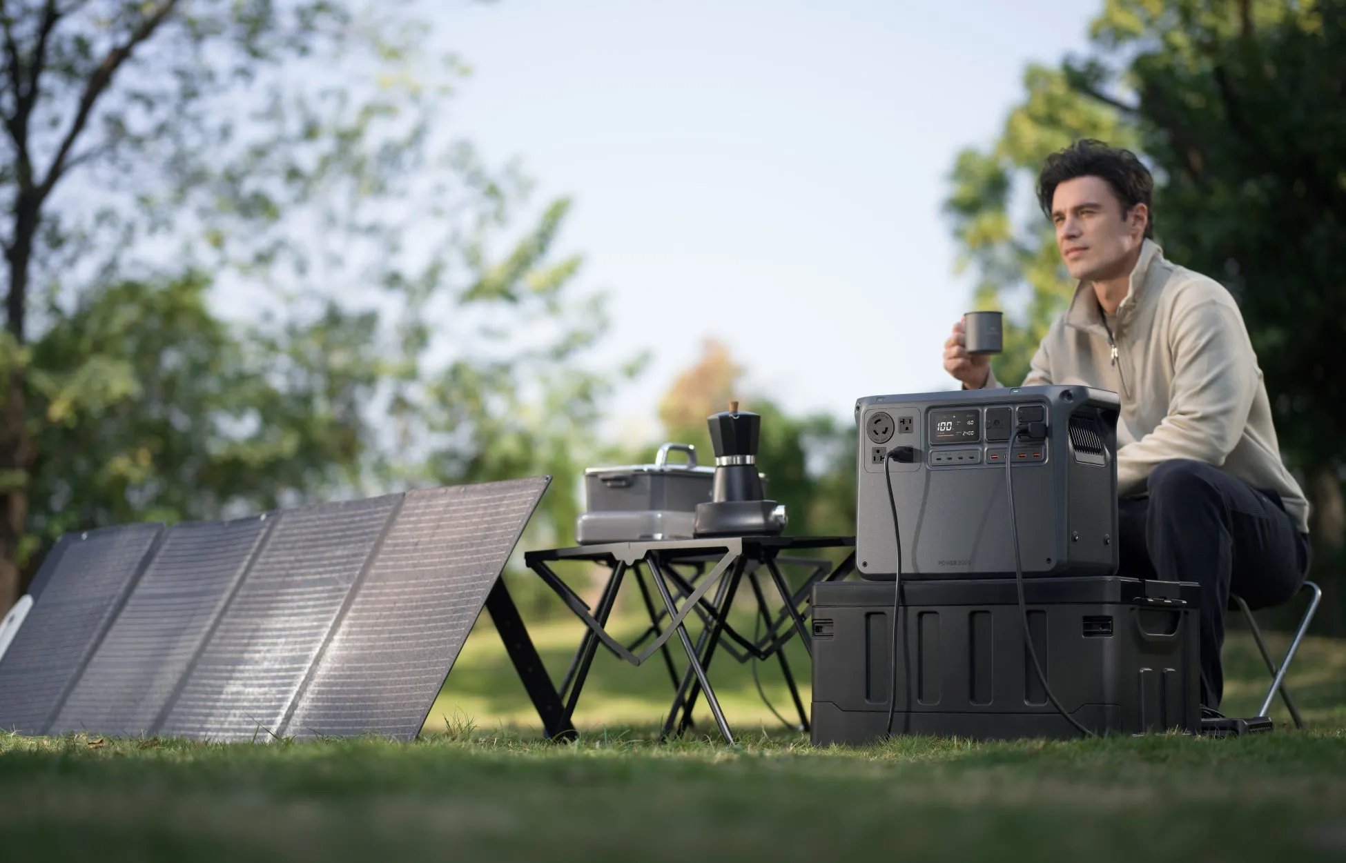 公園でコーヒーを飲みながら、ポータブル電源とソーラーパネルを使用する男性