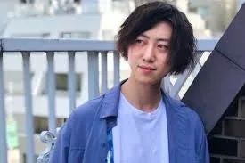 建物の手すりにもたれかかった男性のポートレート。彼はカメラを見ており、日中の屋外で撮影されました。