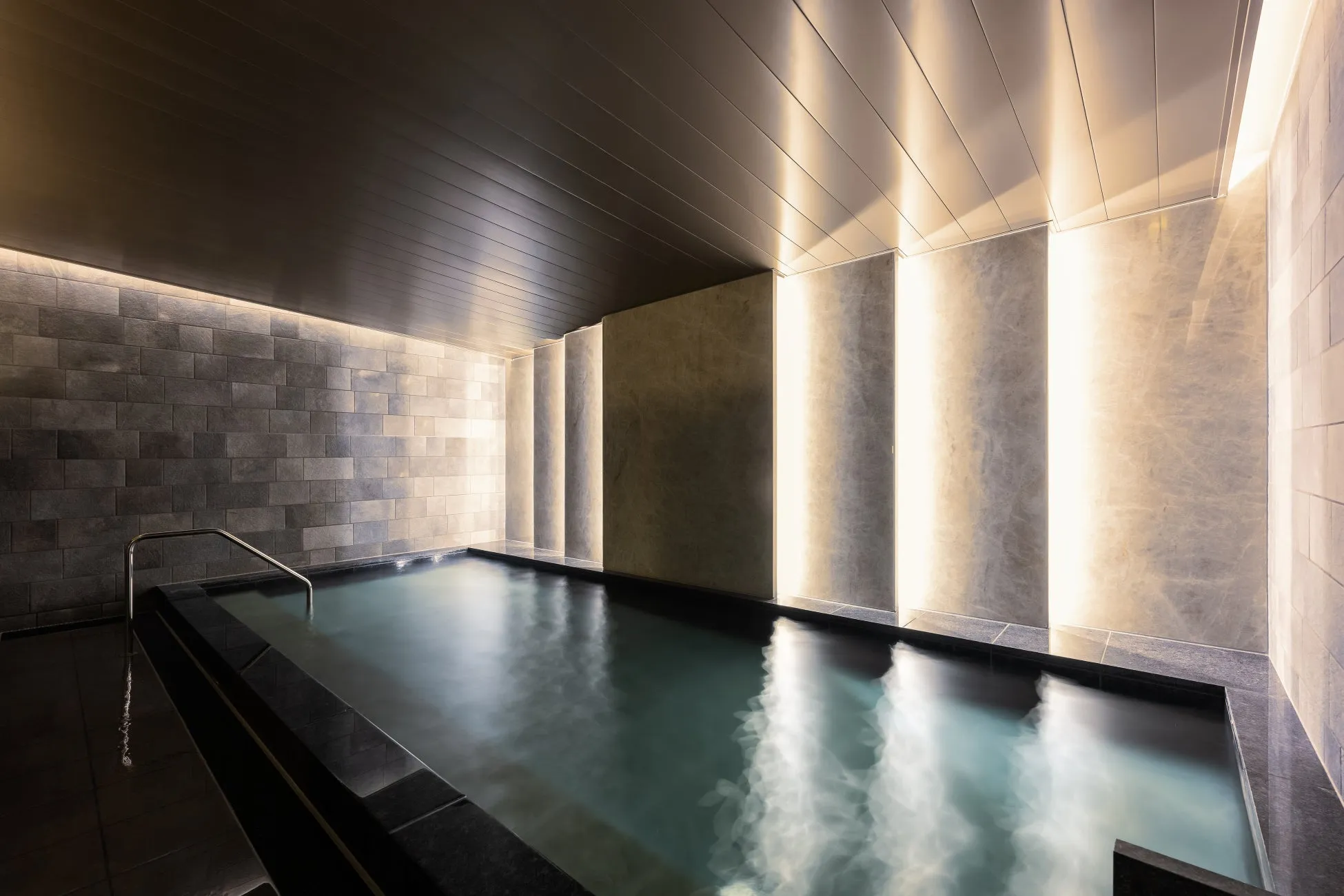 内湯の様子を写した写真。湯気が立ち込める浴槽、間接照明で照らされた壁や天井が特徴的。