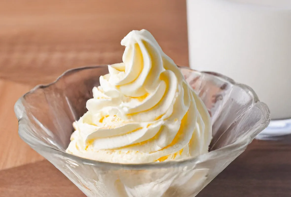 透明なガラスの器に入ったソフトクリーム。バックには、白い液体が入ったグラスが写っている。