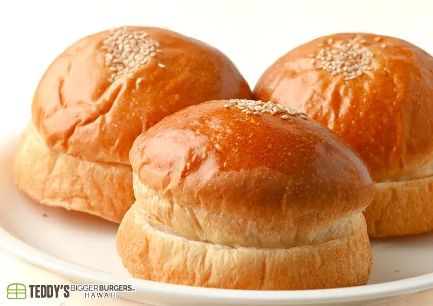白い皿に盛られた、表面がツヤツヤでゴマが散りばめられた3つのハンバーガーバンズのクローズアップ画像です。ふっくらとしていて、食欲をそそる温かい雰囲気が伝わってきます。
