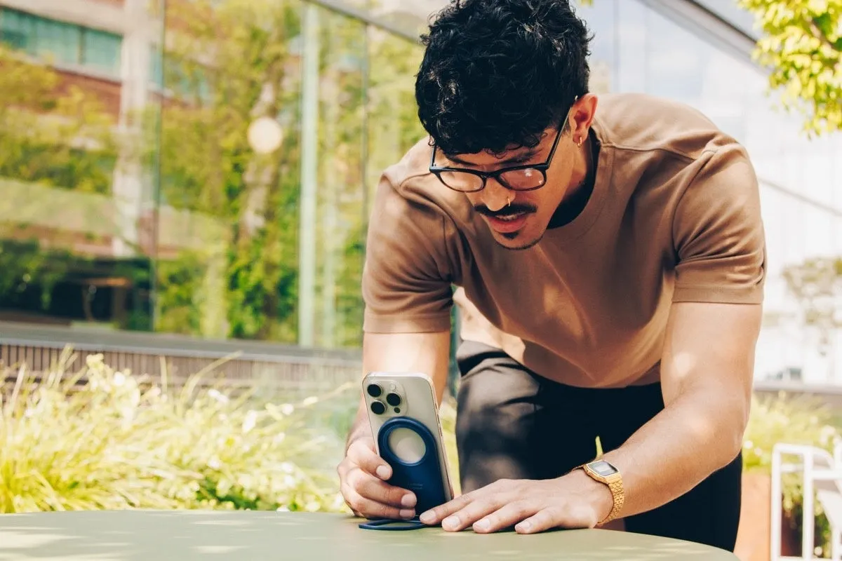 男性が屋外でスマートフォンに何らかのアクセサリーを取り付けている様子。