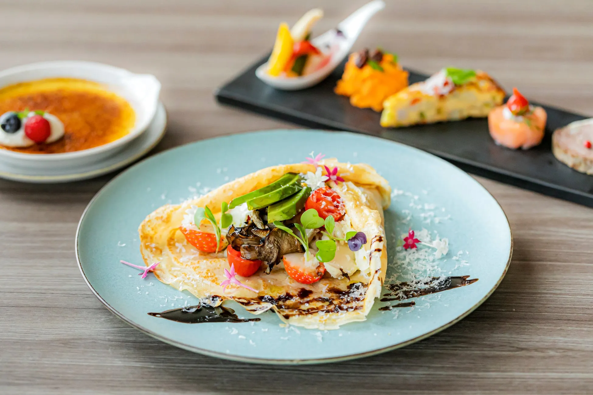 様々な料理が並べられた写真。手前にはクレープ、奥にはブリュレと前菜が写っている。