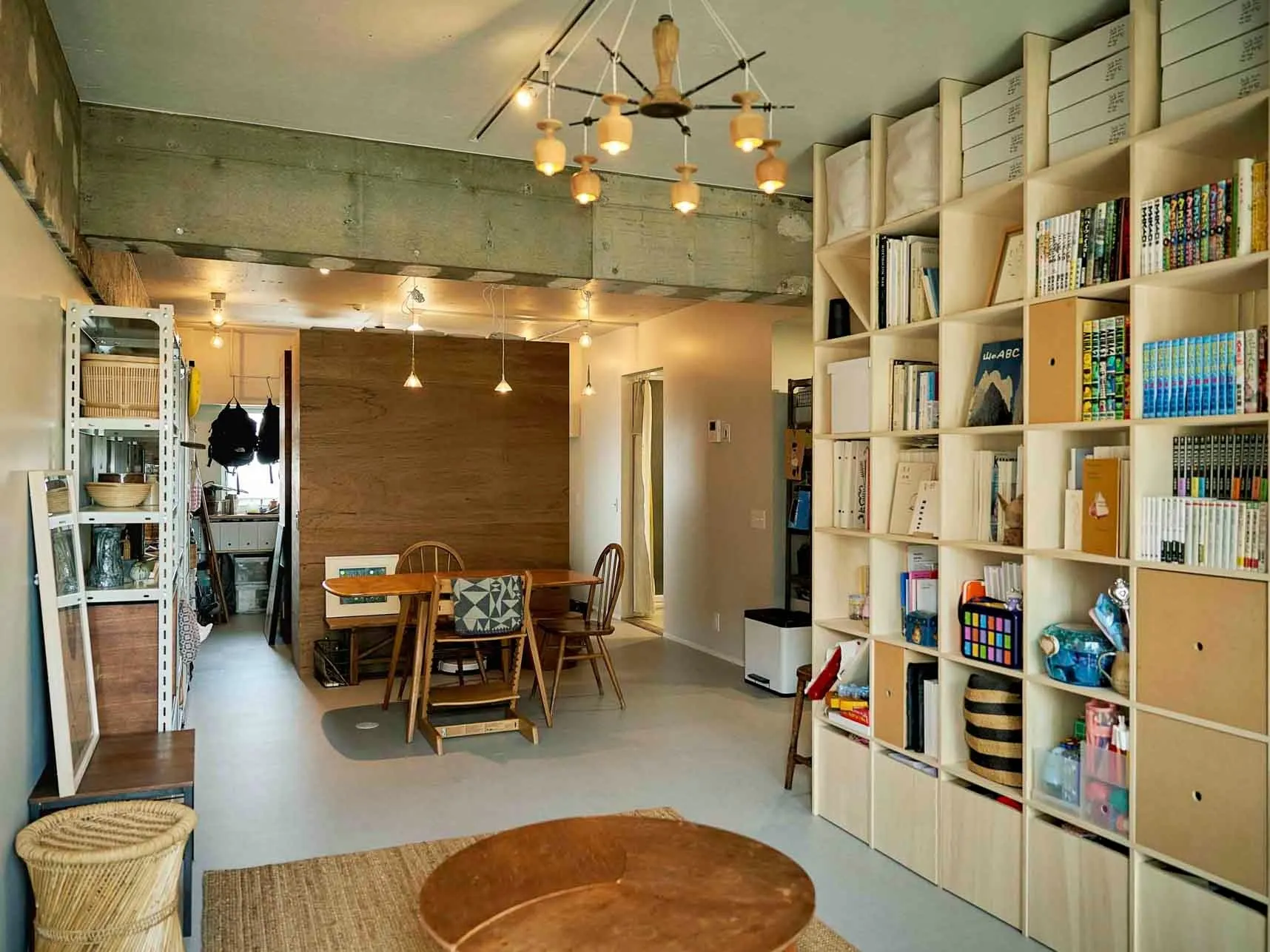 木製の家具が配置されたモダンなリビングルーム。本棚、ダイニングテーブル、丸いコーヒーテーブルなどがあります。