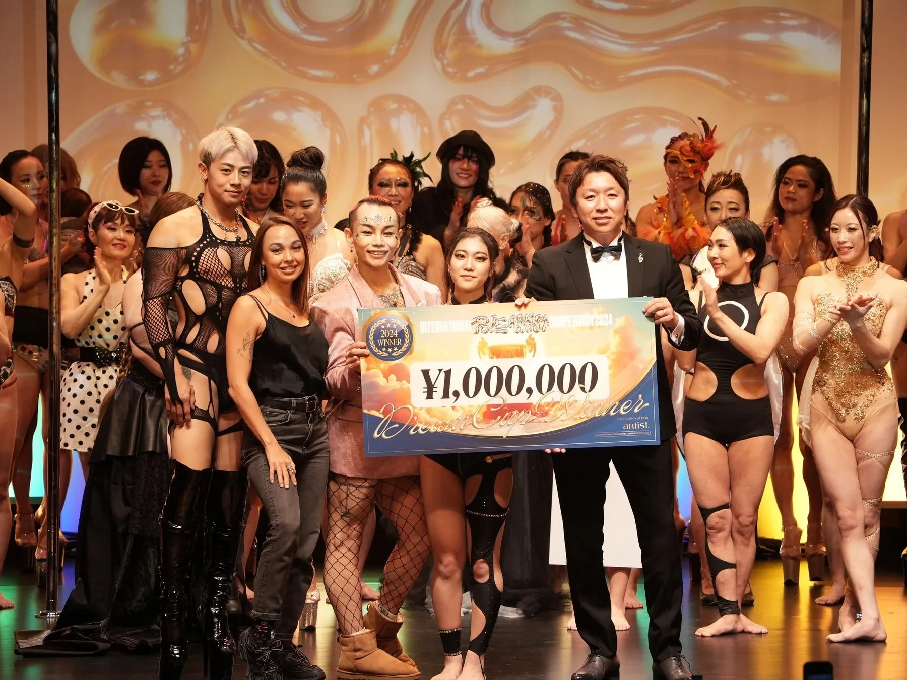 ステージ上で、賞金100万円の小切手を持つ人々のグループの写真。