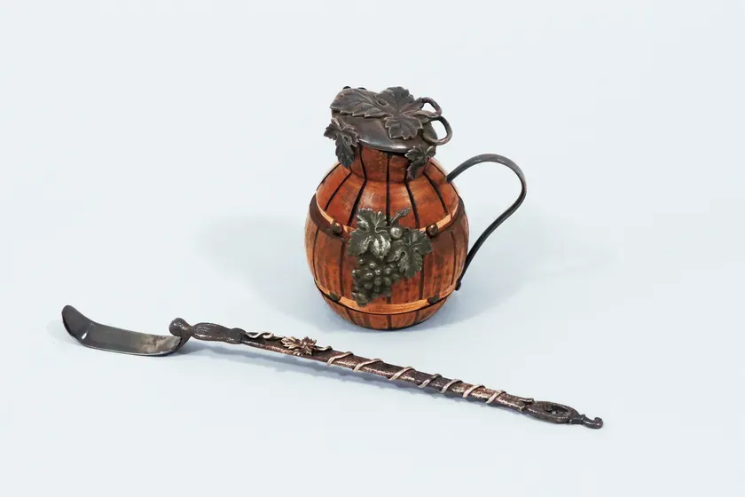 木製の樽型のピッチャーと、葡萄のモチーフが付いたスプーンが写っている画像です。