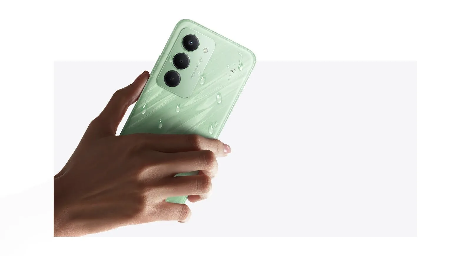 手で持たれた緑色のスマートフォンが写っている画像。スマートフォンの背面には3つのカメラがあり、水滴がついている。背景は白。