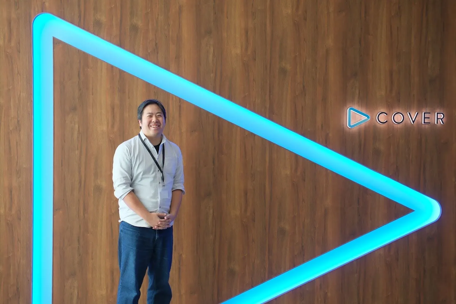 木目調の壁の前に立つ男性の画像