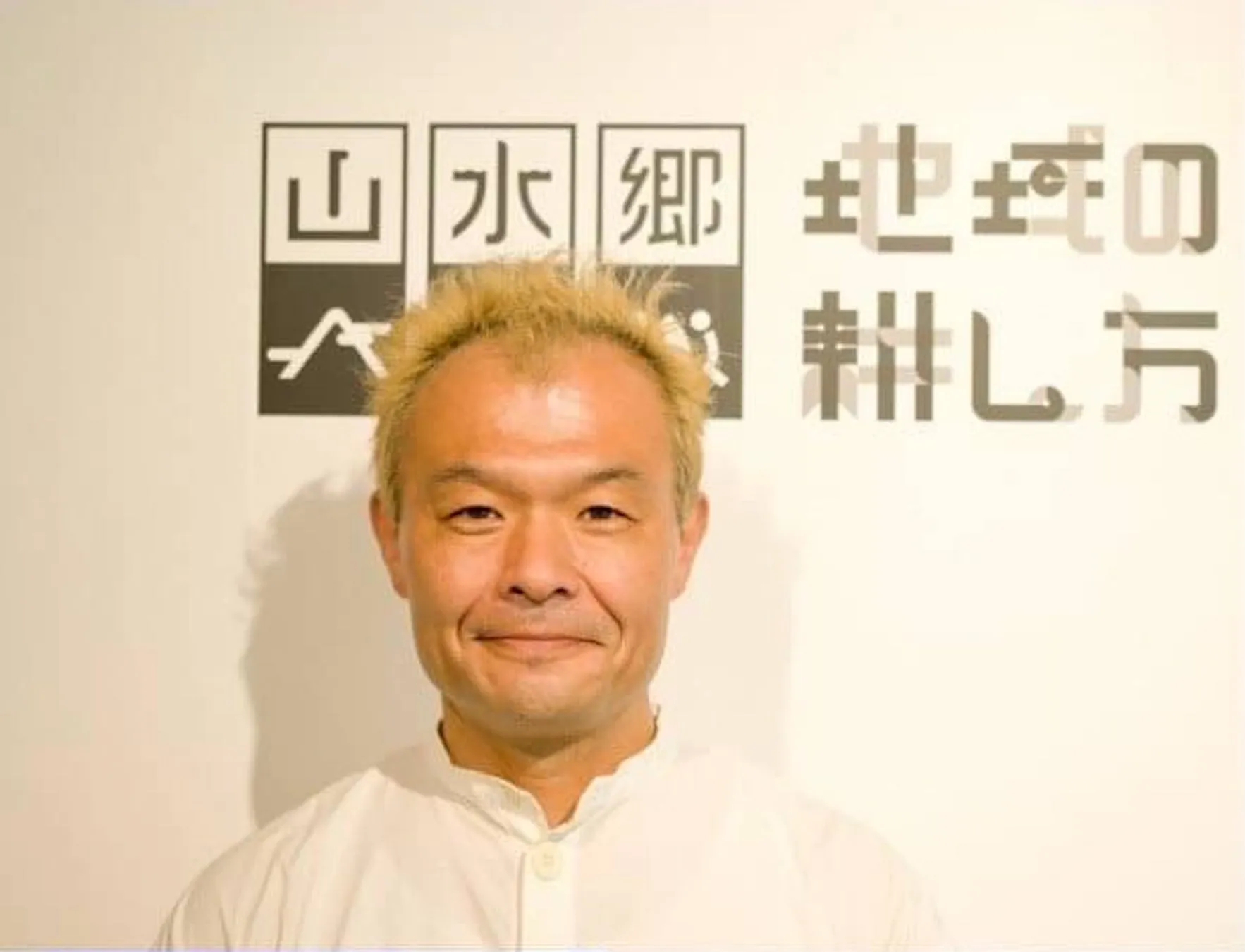 男性が写っている写真。背景には「山水郷　地域の耕し方」と書かれた看板がある。