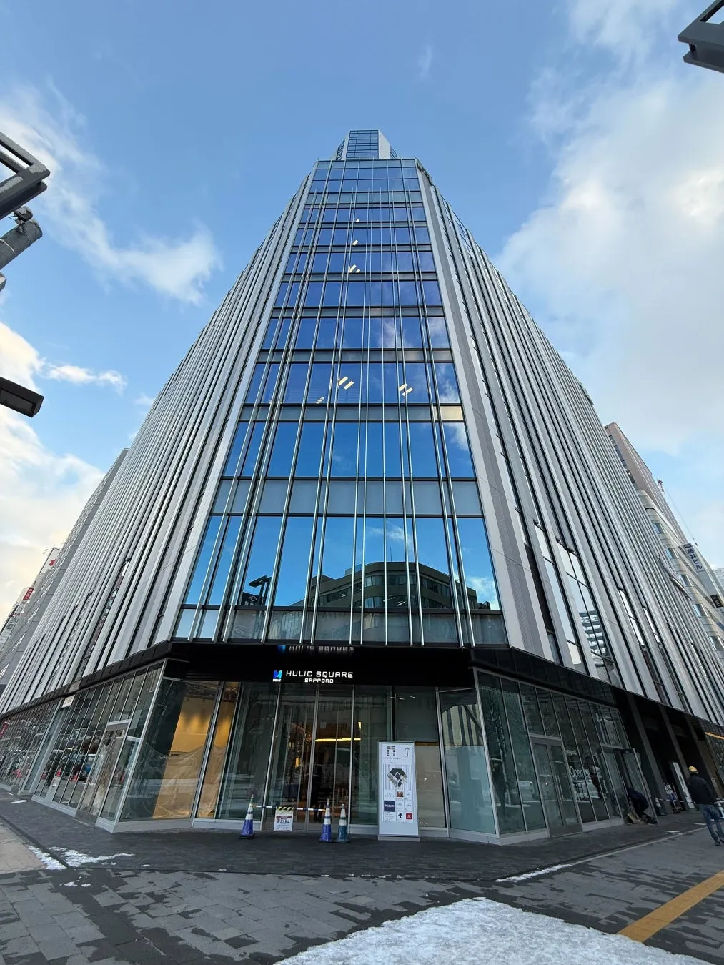 札幌のHULIC SQUAREビルの外観を捉えた写真です。青空の下、ガラス張りの近代的な建物がそびえ立っています。