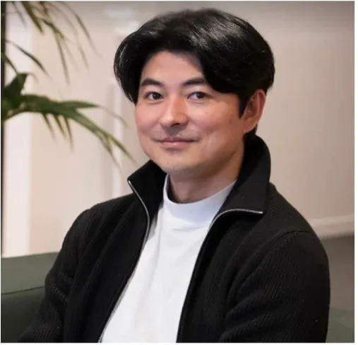 黒いジャケットと白いタートルネックを着た、東洋人の男性のポートレートです。彼は穏やかな表情をしています。