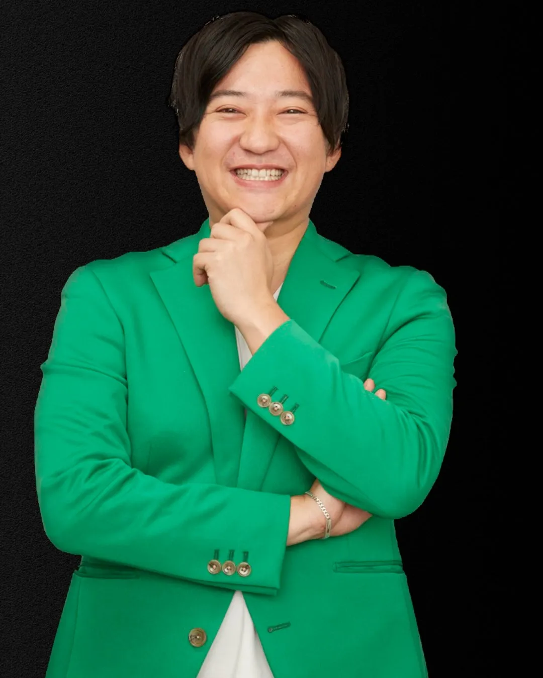 緑のジャケットを着た笑顔の男性のポートレート。男性は顎に手を当てており、カメラ目線で微笑んでいる。