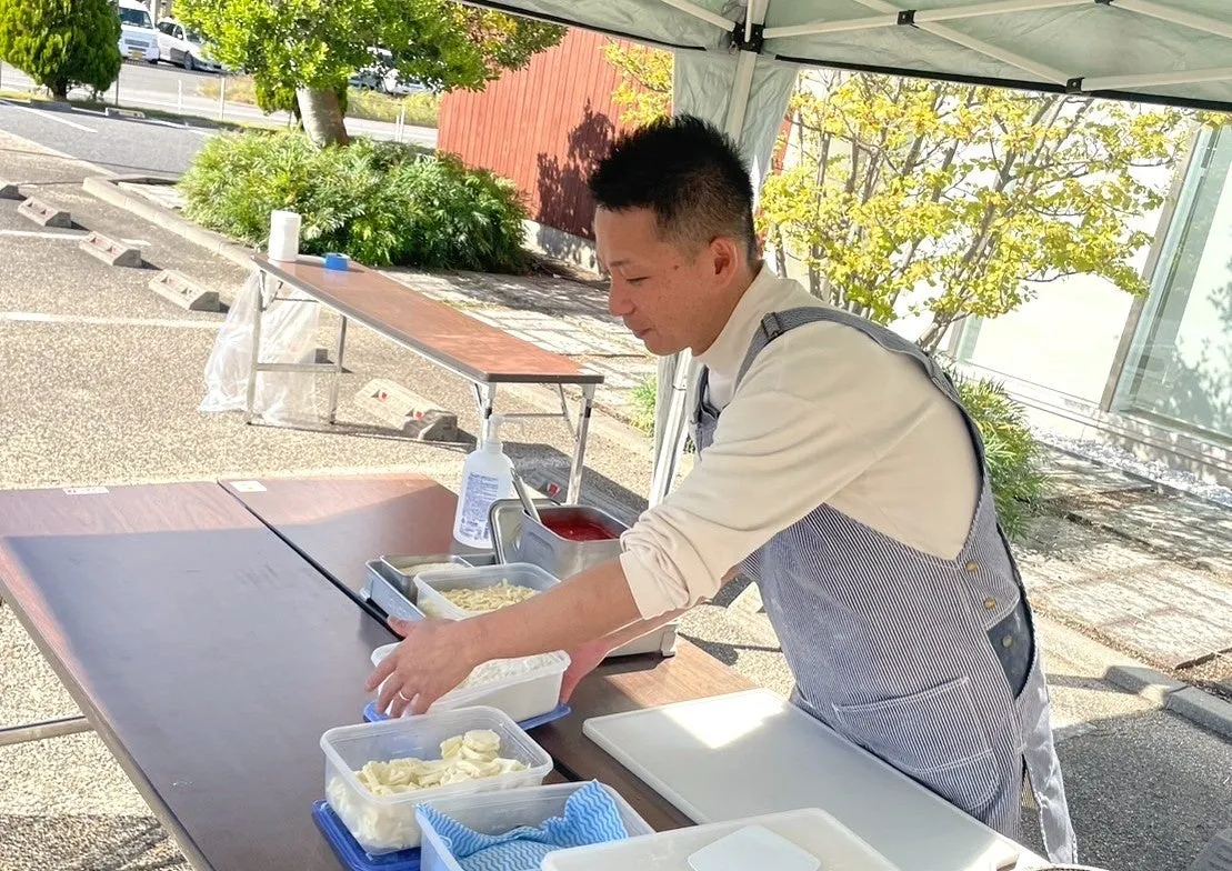 男性が屋外で調理の準備をしている様子。食材や調理器具がテーブルに並べられ、彼は料理に集中している。
