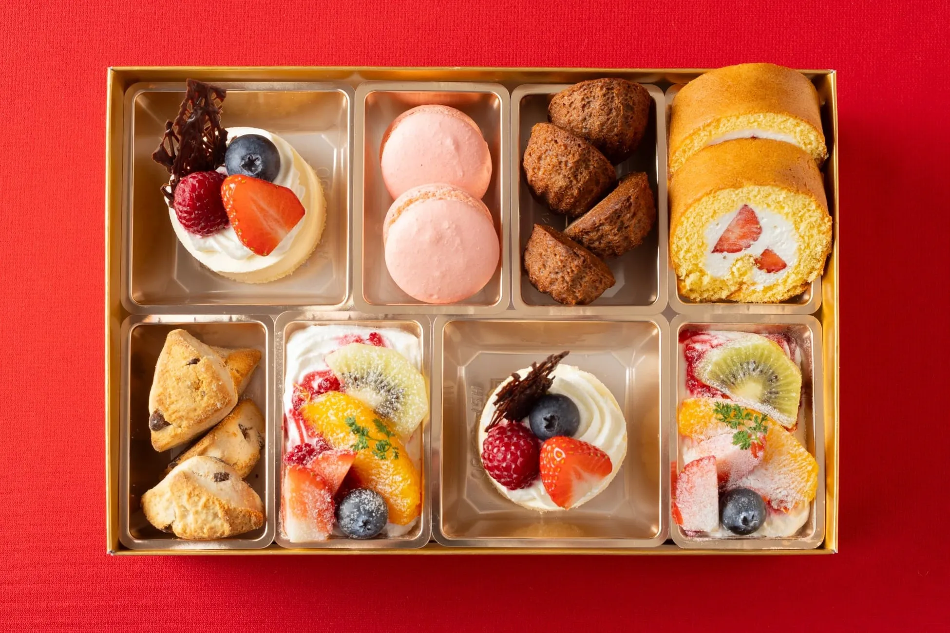 様々なお菓子が詰め合わせになった画像です。チーズケーキ、マカロン、焼き菓子、ロールケーキ、フルーツが美しく配置されています。