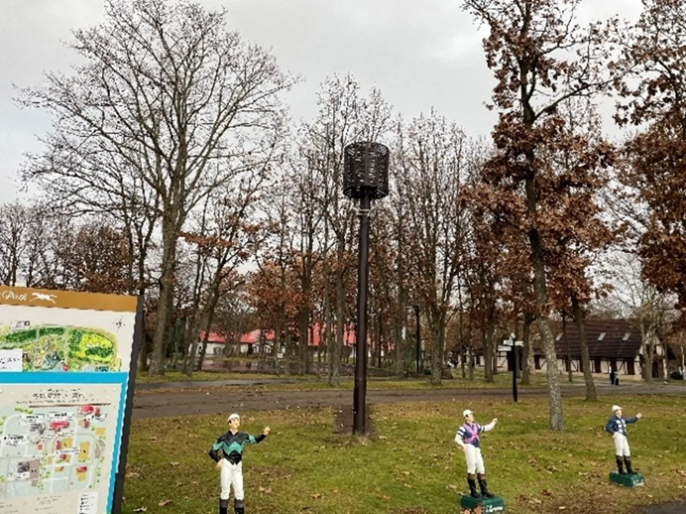 公園の風景写真。手前に地図と騎手の像があり、奥には木々や建物が見える。空は曇り空。