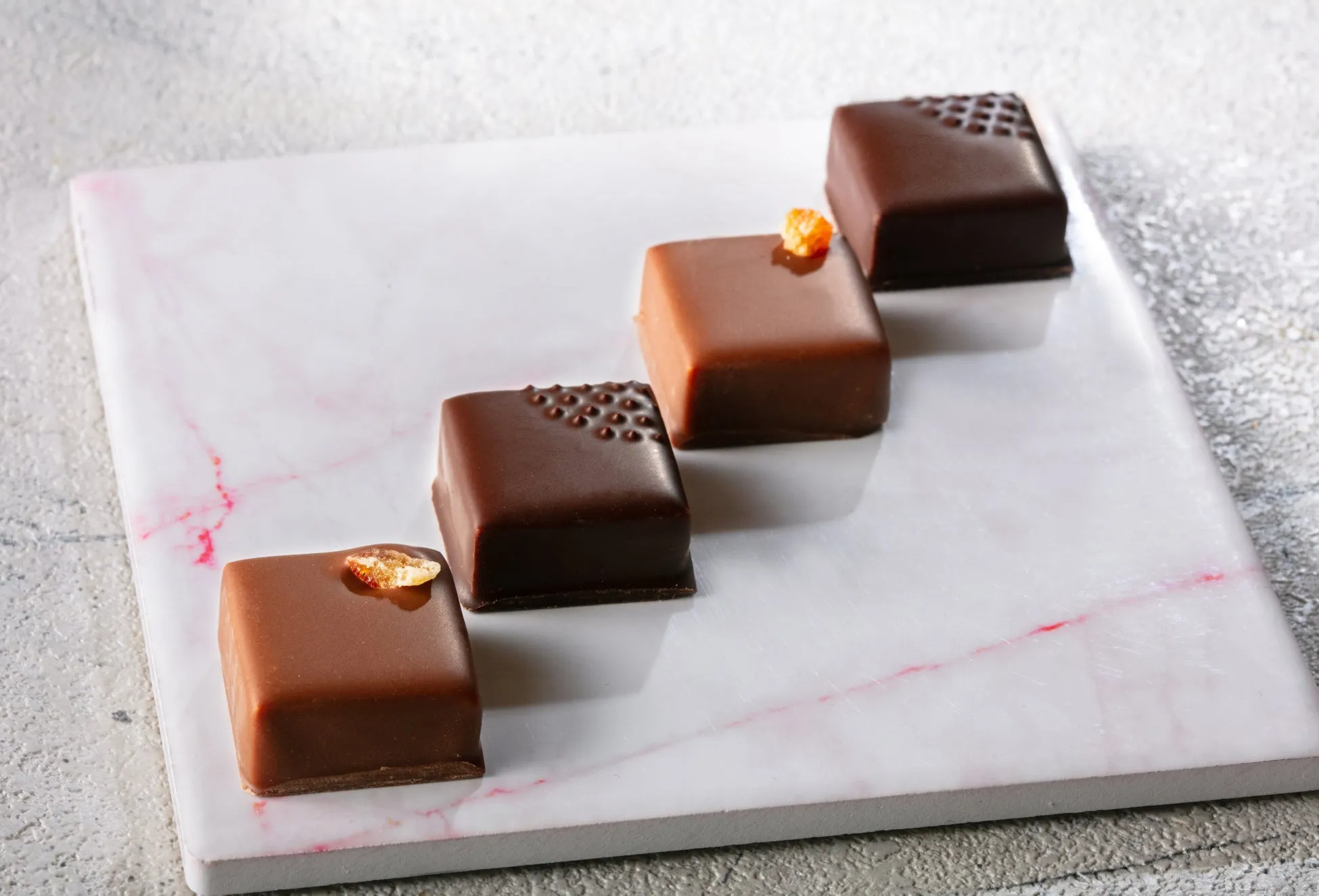 大理石の板の上に、4つのチョコレートが並んでいる画像。チョコレートには、それぞれ異なる装飾が施されている。