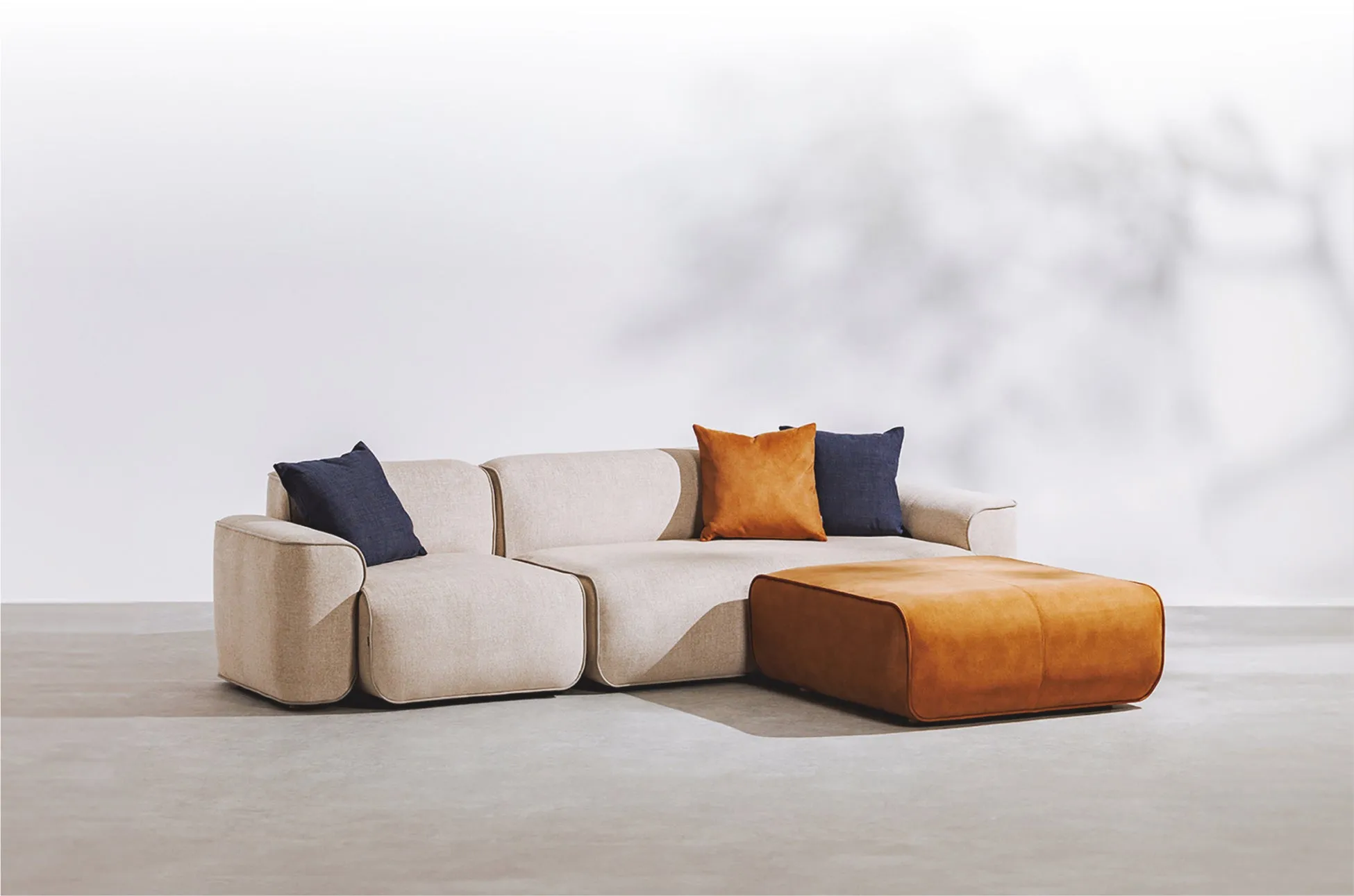 明るいベージュのモダンなL字型ソファとオレンジ色のオットマンが配置されたリビングルームの画像です。ネイビーとオレンジのクッションがアクセントになっています。シンプルで快適な空間を演出しています。