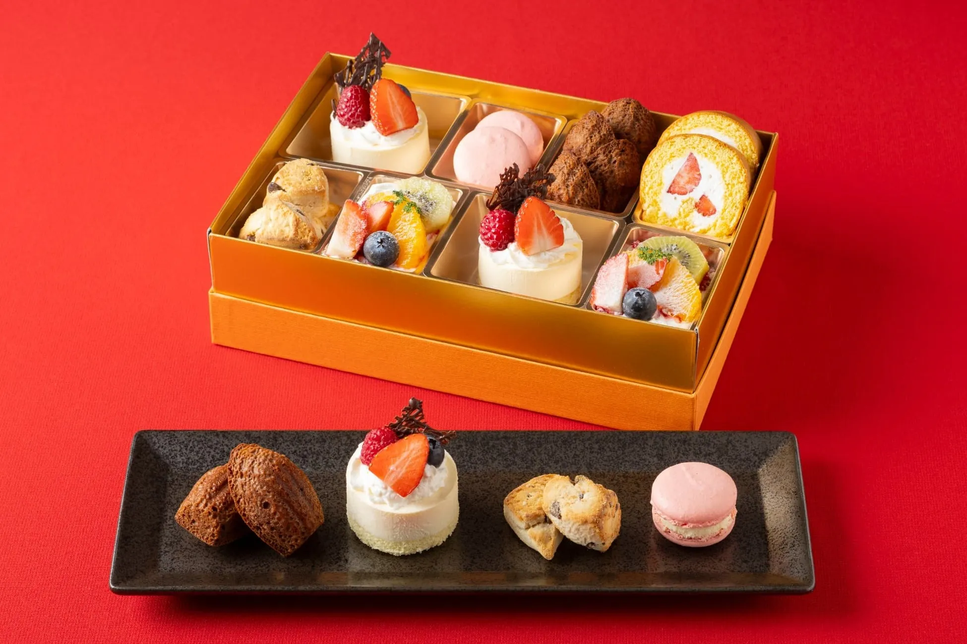 様々なお菓子が詰め合わされたギフトセットの画像。ケーキ、マフィン、マカロン、フルーツなどが含まれている。