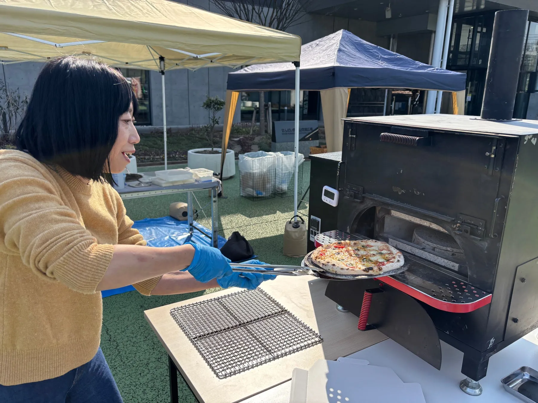 女性が屋外でピザを焼いている様子。ピザ窯から焼きあがったピザを取り出している。