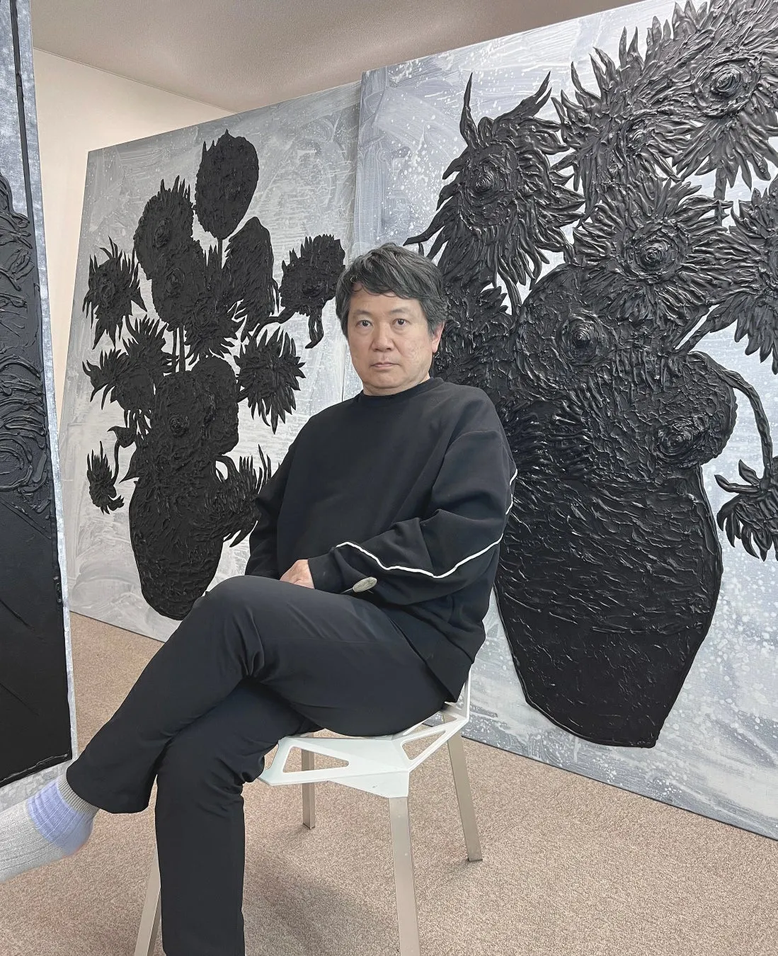 男性が椅子に座り、黒いひまわりの絵の前に立つ