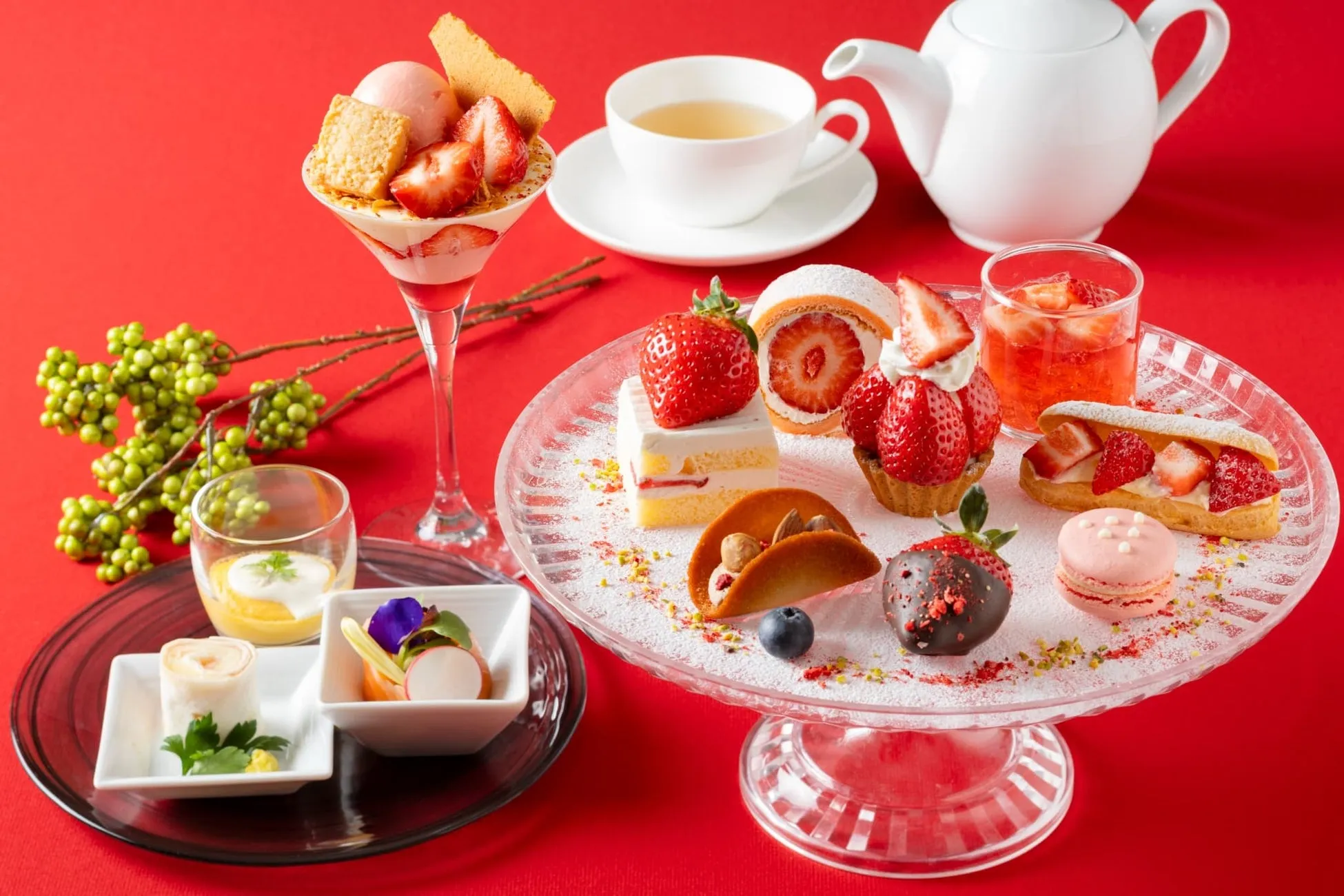 様々なデザートが並んだアフタヌーンティーの画像です。イチゴをメインに、ケーキ、タルト、マカロン、パフェ、ロールケーキ、チョコレート、紅茶が写っています。