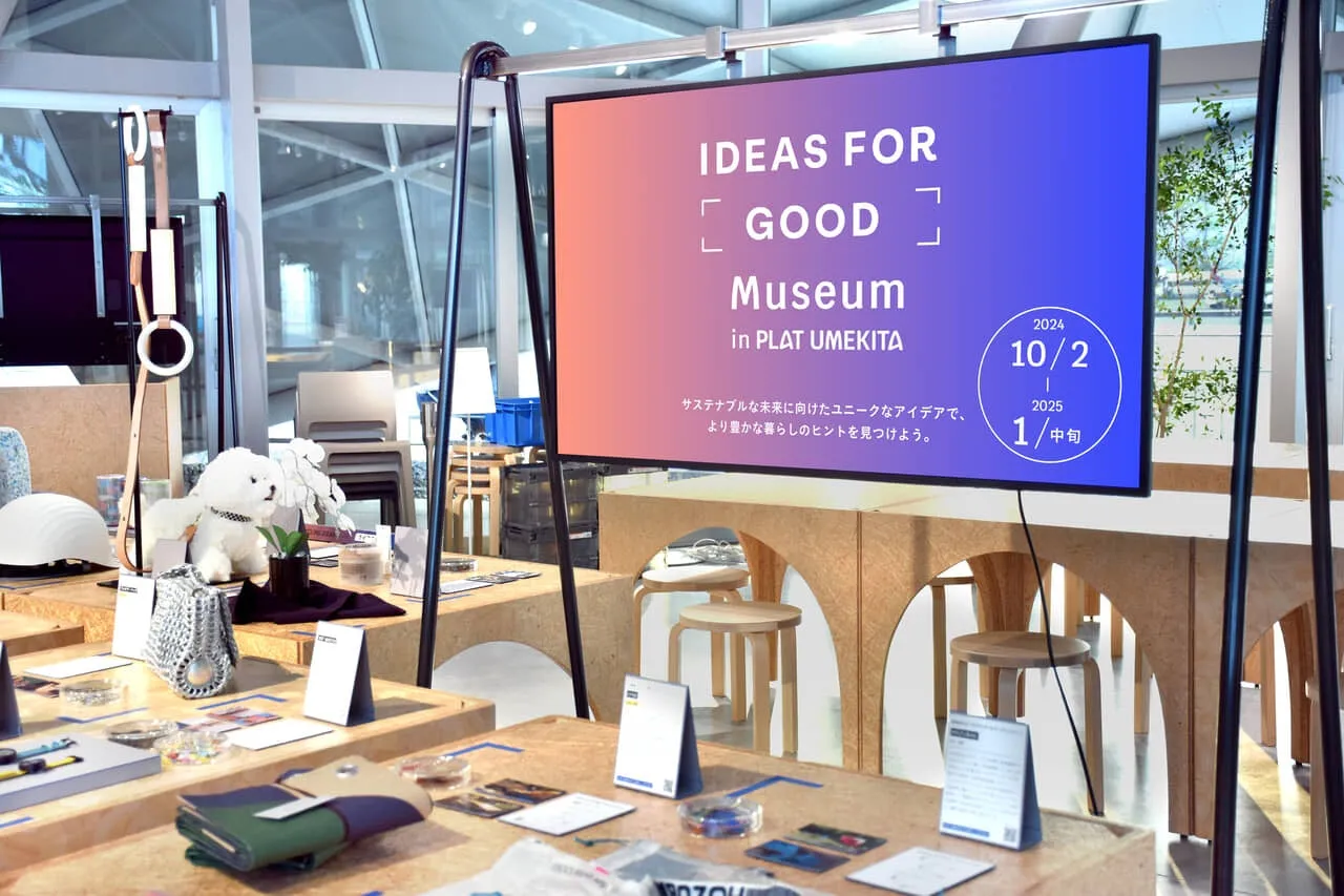 展示会の様子。スクリーンには「IDEAS FOR GOOD Museum in PLAT UMEKITA」という文字と開催期間が表示されている。テーブルの上には様々な商品が並べられている。