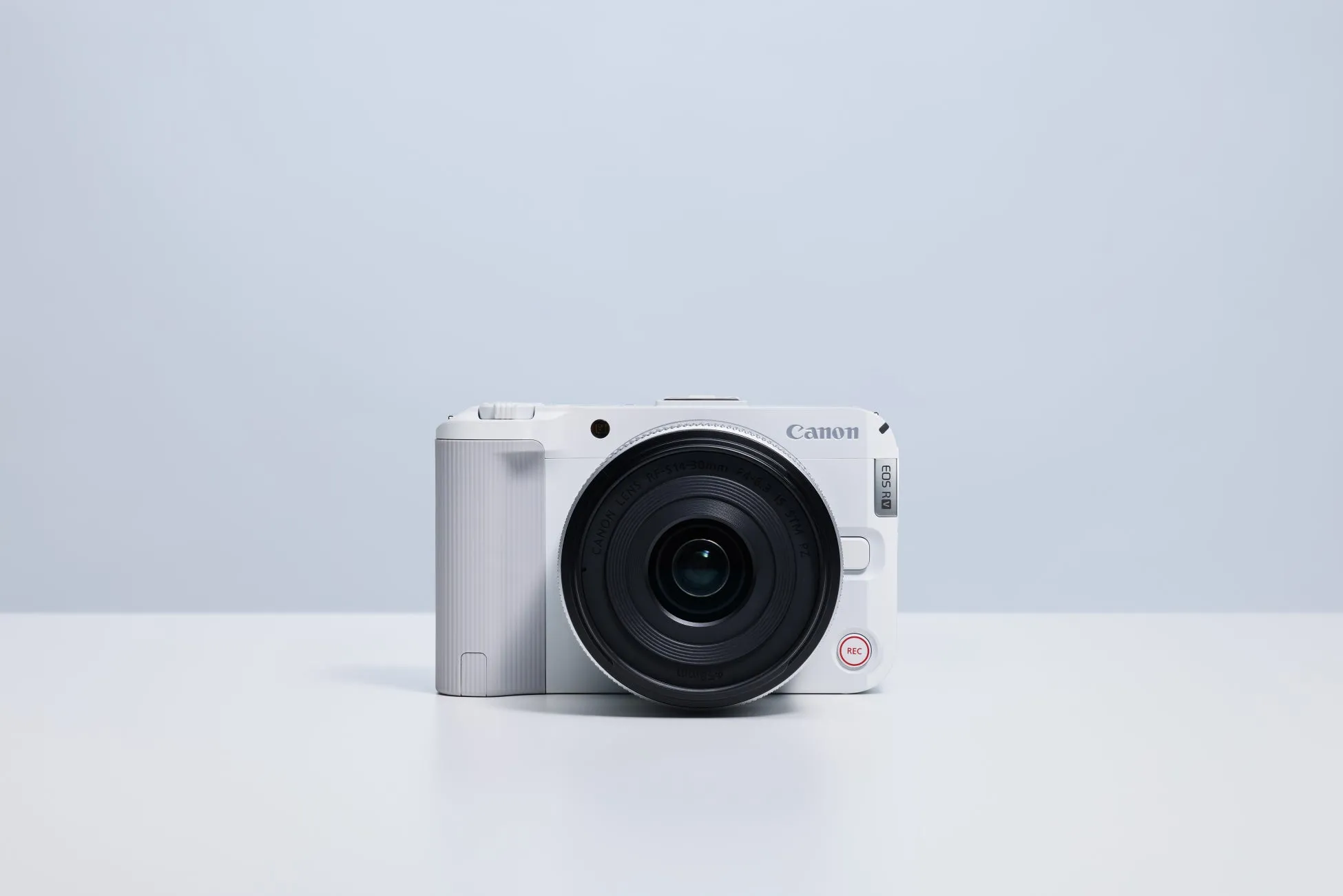 白いCanon EOS Rカメラのクローズアップ写真。カメラは白いテーブルの上に置かれ、背景は明るい青色です。