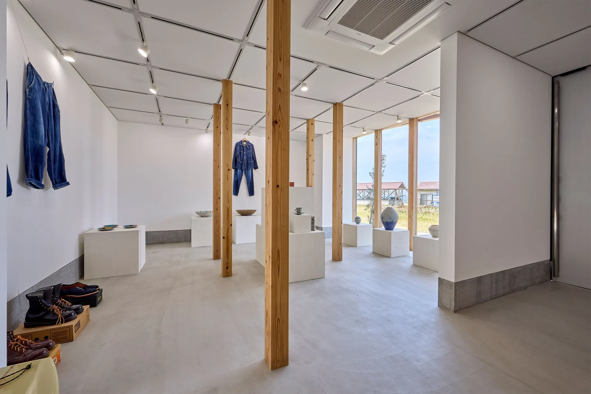 木製の柱が並ぶギャラリー。壁にはデニムの服が飾られ、展示台には陶器や靴