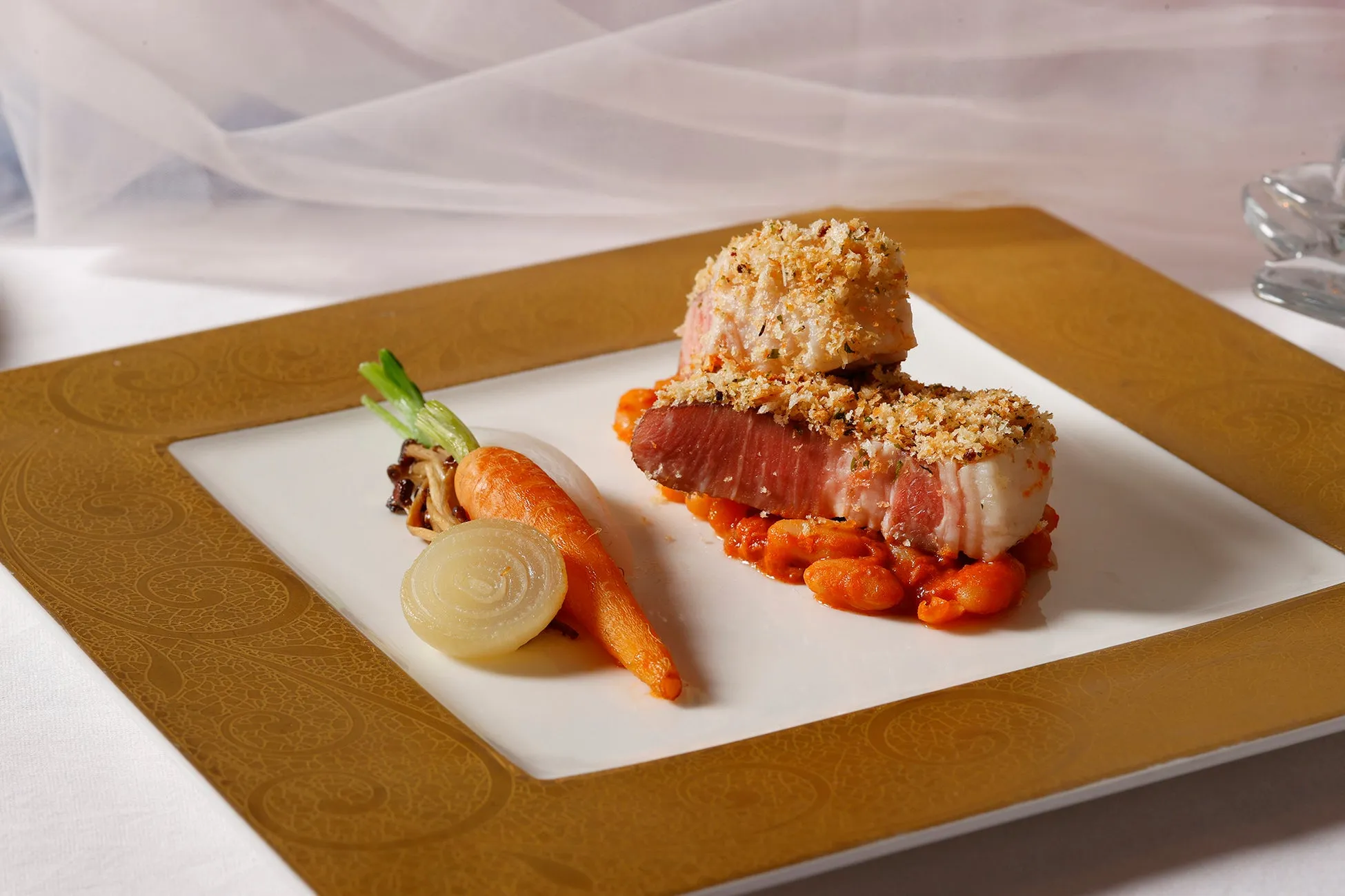 お皿に盛られた料理の写真。メインディッシュは、衣をまとった肉料理で、トマトソースと豆の上に配置されている。付け合わせとして、ニンジン、タマネギ、キノコが添えられている。