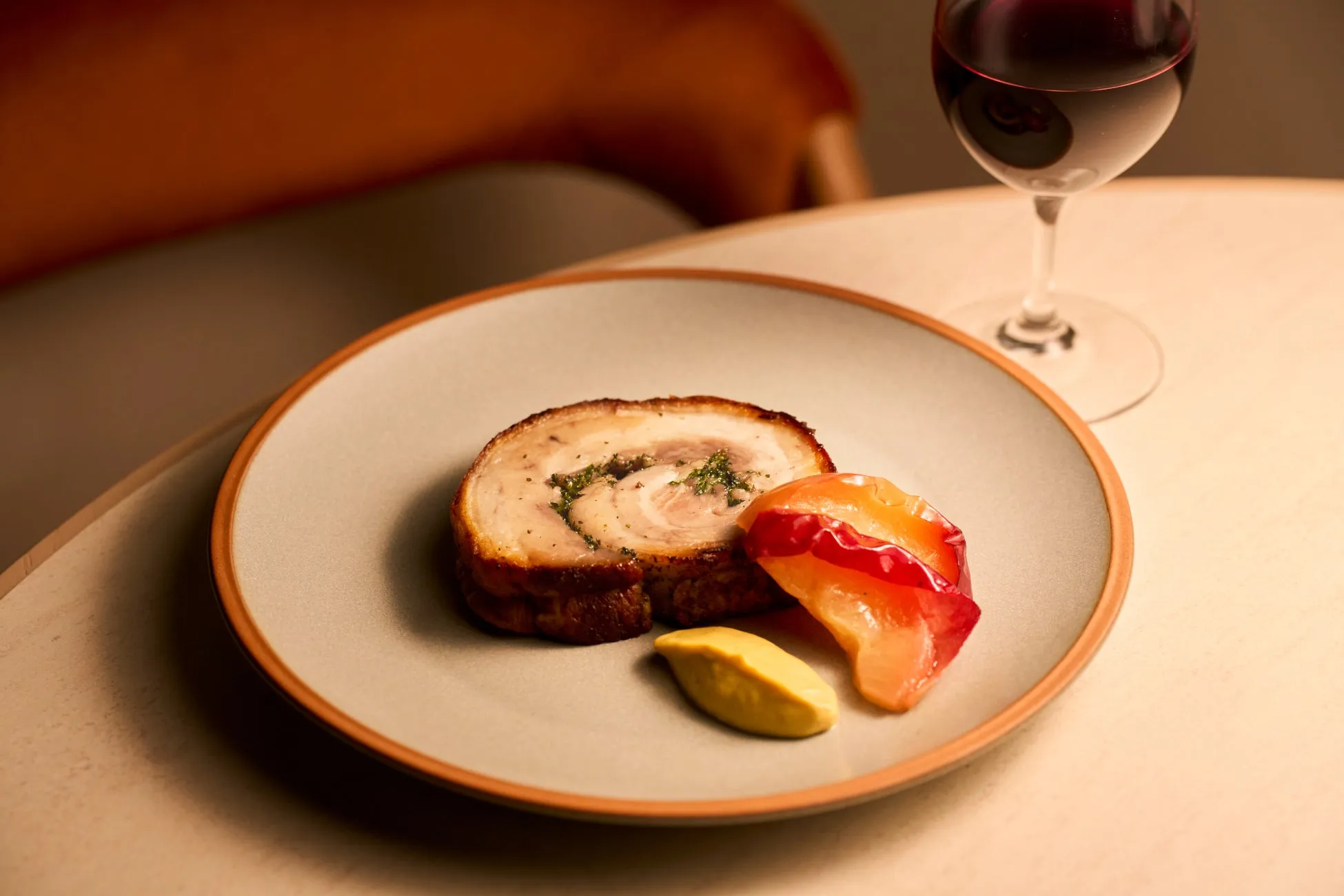 お皿に盛り付けられた料理。ローストされた豚肉の塊、添えられたソースと果物、そしてグラスに入った赤ワインが写っています。
