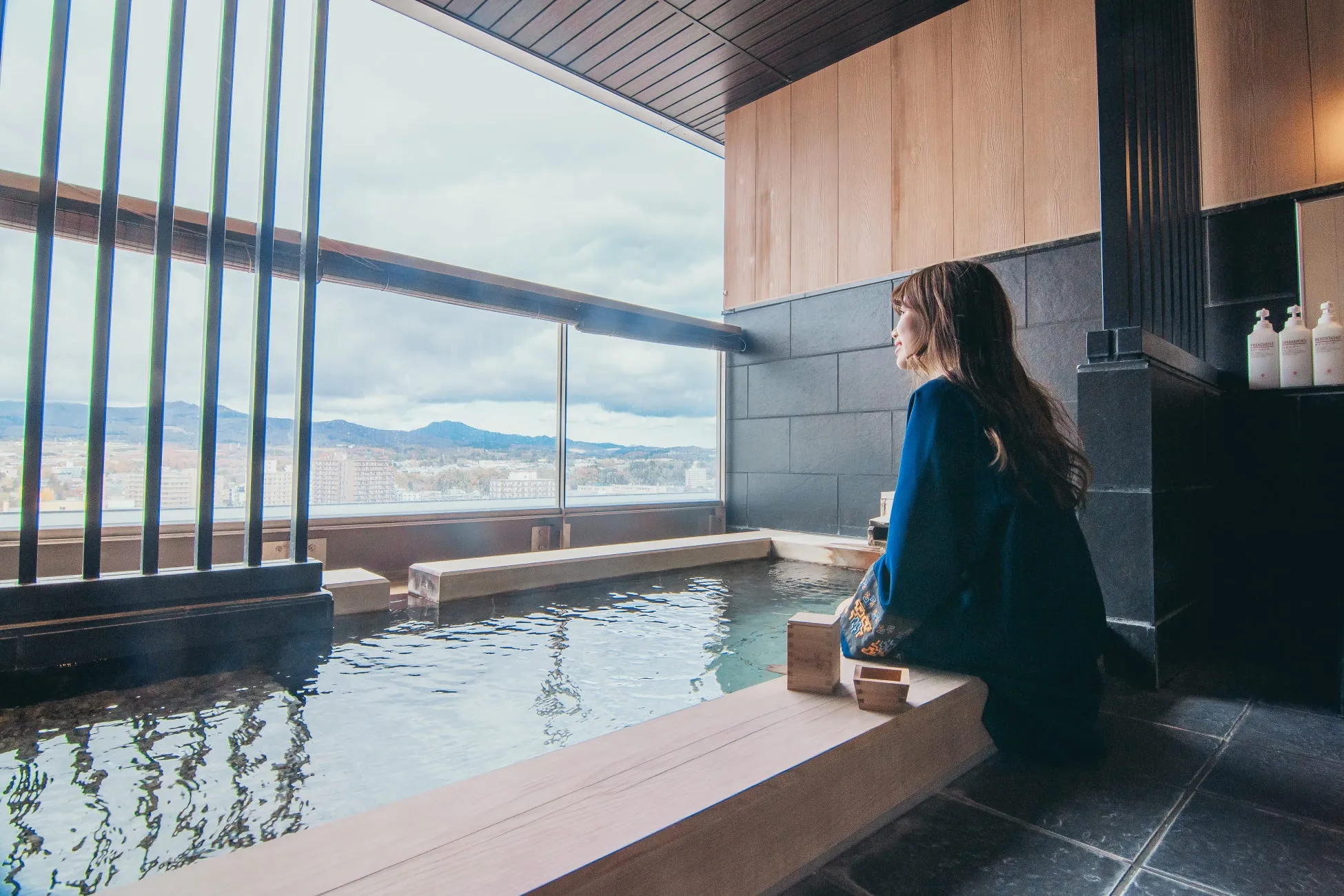 露天風呂に入り、窓の外の景色を眺める女性