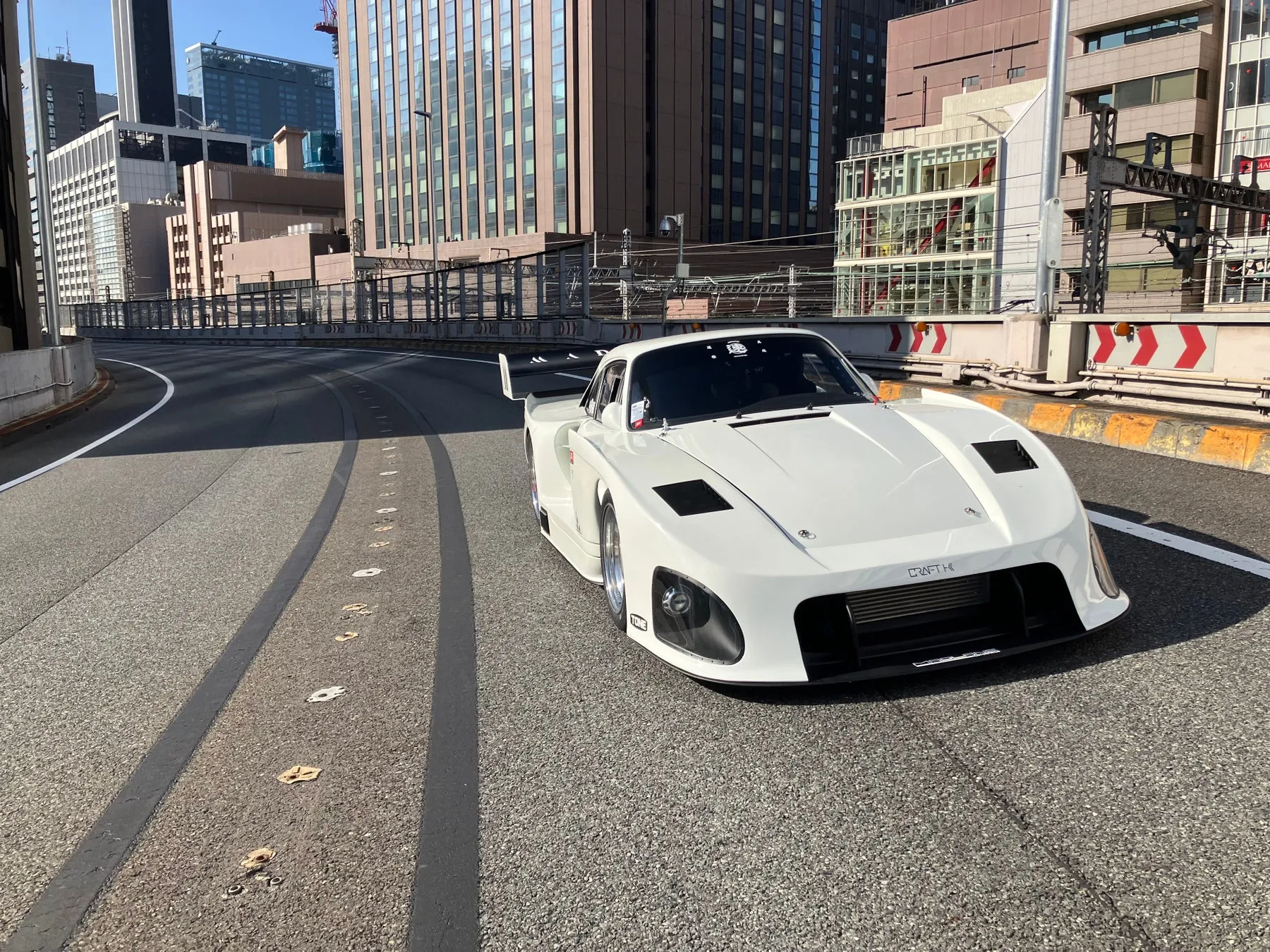 白い車が道路を走っている写真。背景には高層ビルが立ち並び、都市の風景が広がっている。