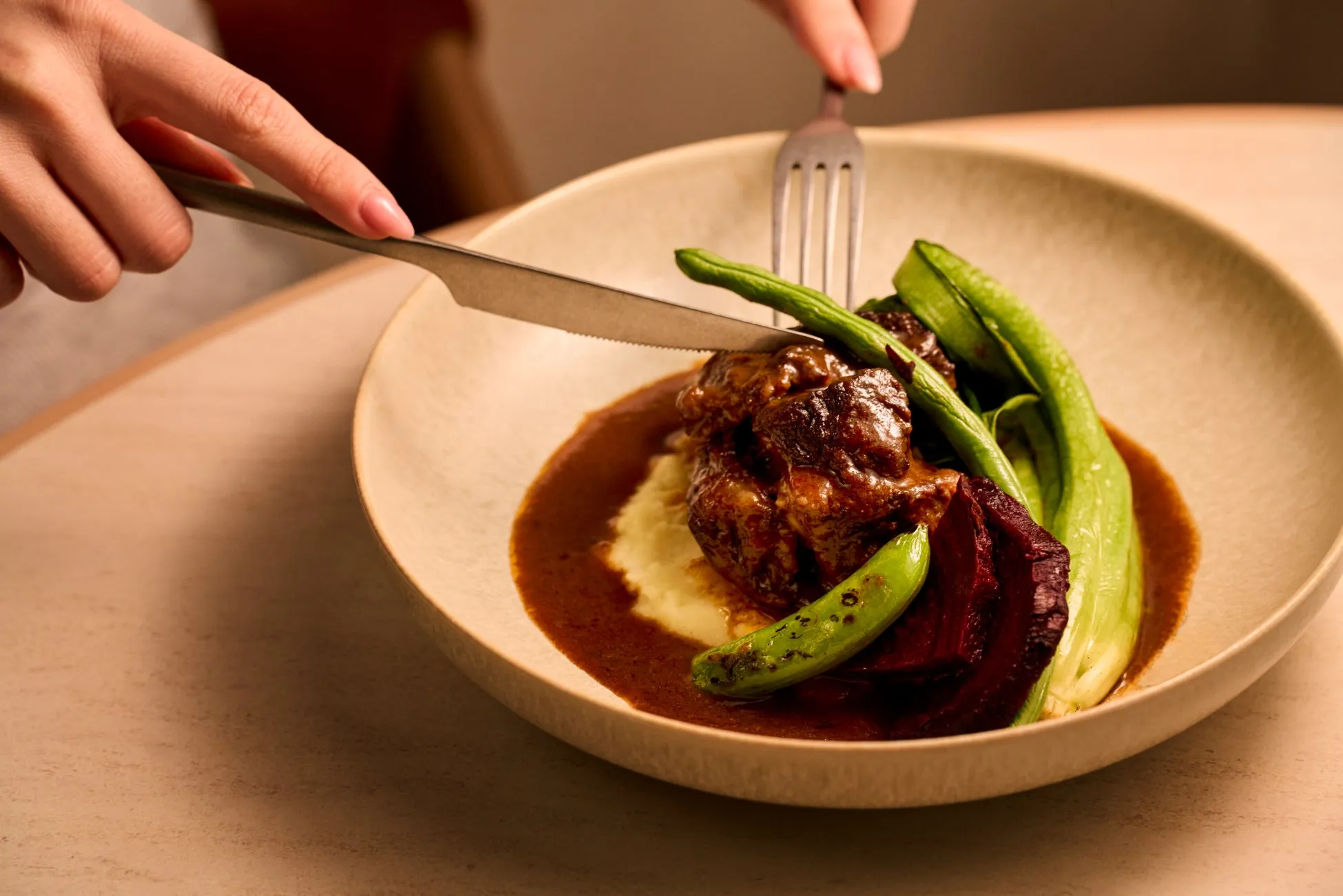 お皿に盛られた料理をナイフとフォークで食べる様子。メインは肉料理で、付け合わせに豆や野菜が添えられている。