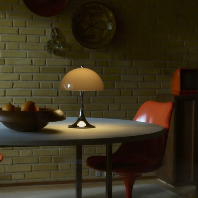 テーブルの上に置かれたランプのクローズアップ。オレンジ色の椅子とオレンジ色のフルーツが入ったボウルがテーブルに置かれています。レンガの壁には装飾品が飾られています。
