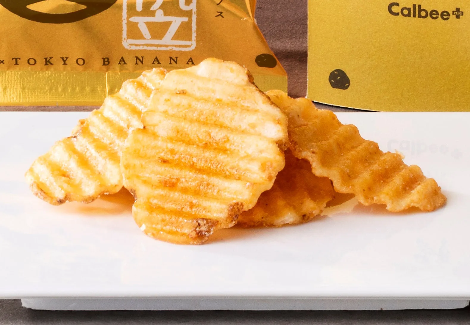 白いお皿に、カルビーのポテトチップスがいくつか重なって置かれています。奥にはTOKYO BANANAのパッケージが見えます。