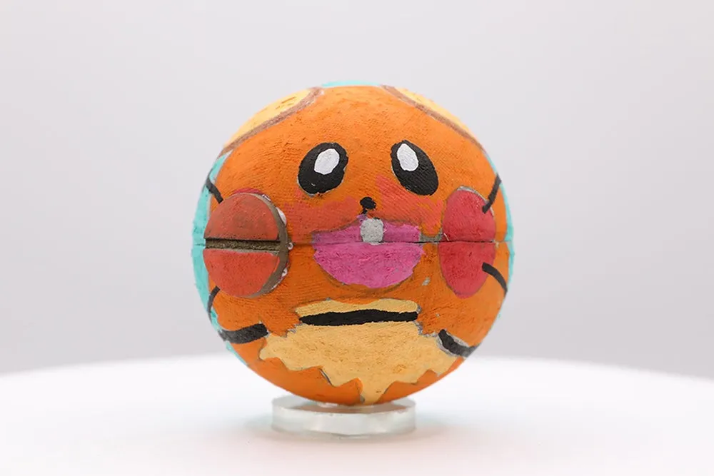 丸い物体にキャラクターの顔が描かれた写真です。オレンジ色を基調とし、目や口、頬が描かれています。水色の部分も少しあります。