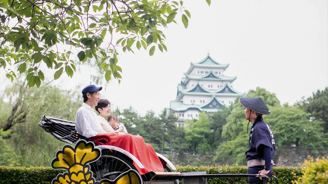 名古屋城を背景に人力車に乗る家族の写真です。父親、母親、赤ちゃんが乗っており、人力車の車夫が前に立っています。
