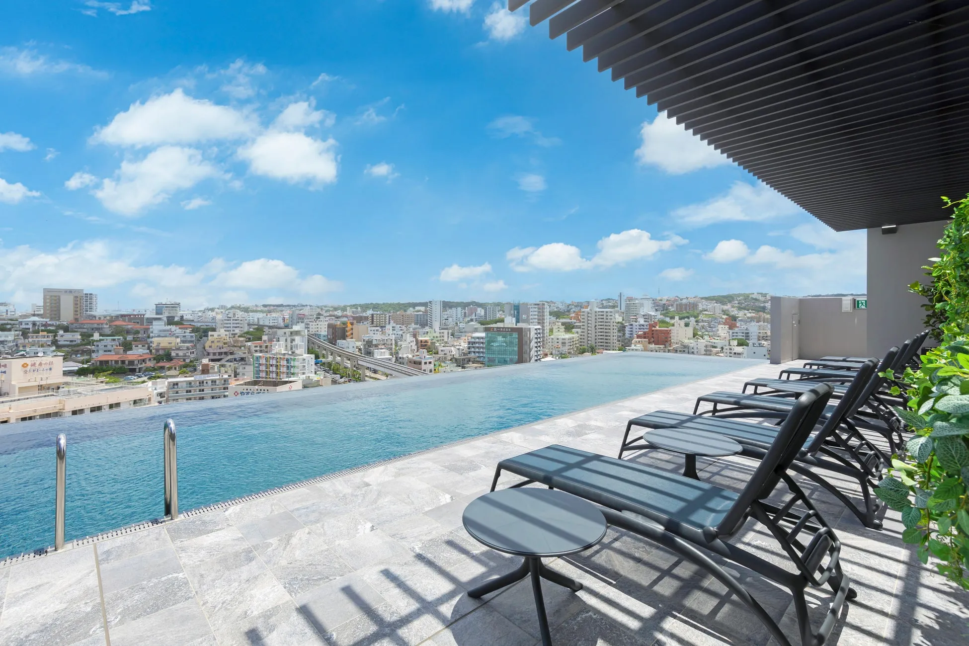 屋上プールと街並みの写真。青空の下、屋上プールにはデッキチェアが並び、遠くには市街地が見える。